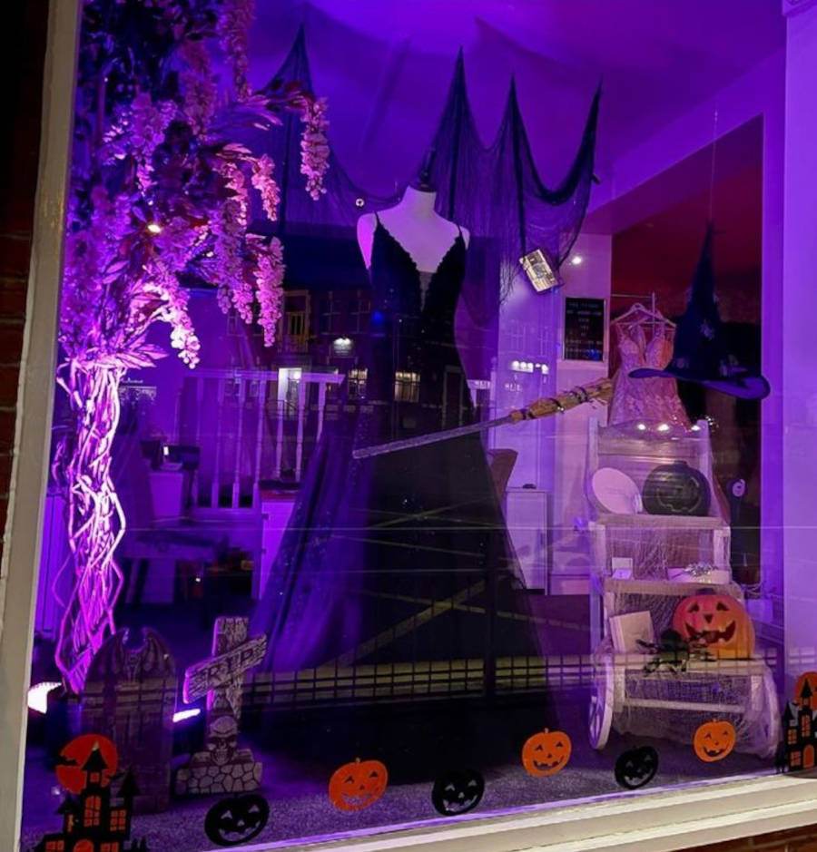 Foto de uma vitrine de Halloween de loja de vestido iluminada com luzes roxas e enfeitos típicos de Halloween