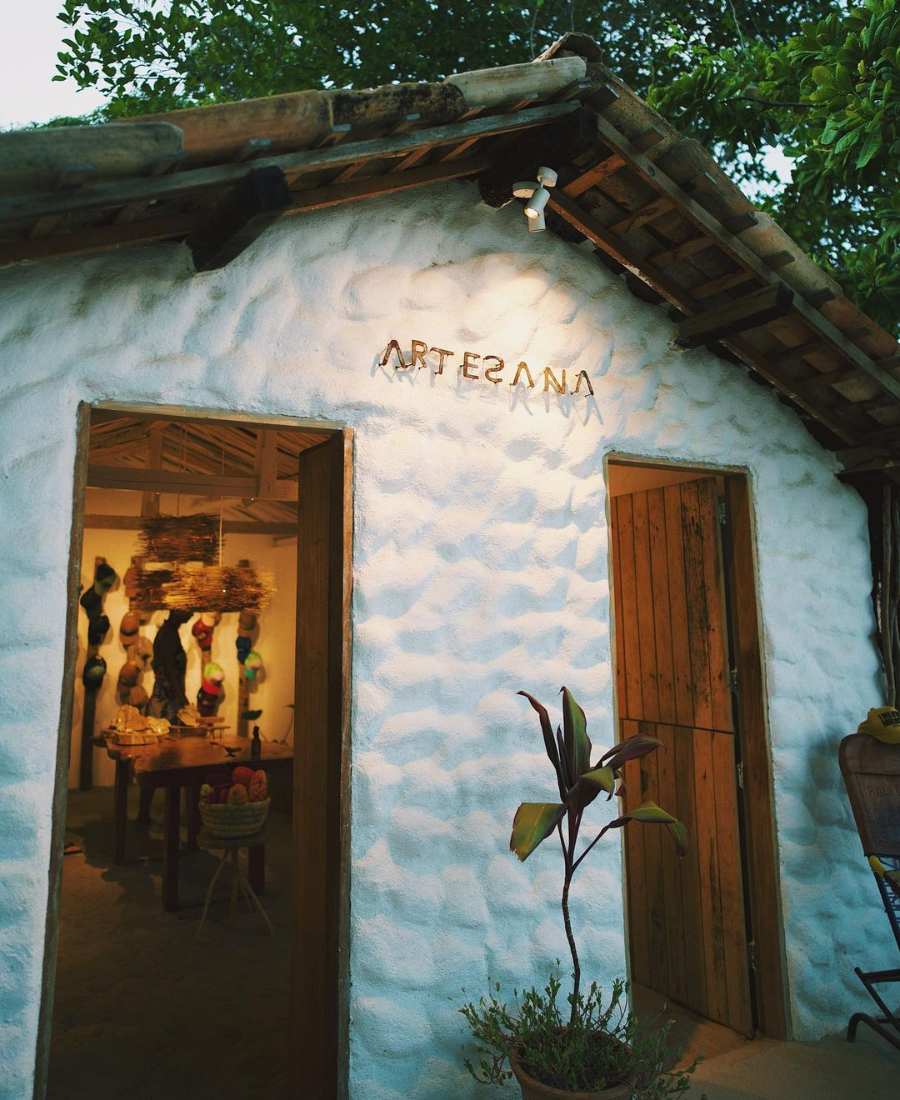 Foto da entrada do ateliê. Casa com fundo de árvore, entrada com duas portas, e vaso com planta no meio delas.