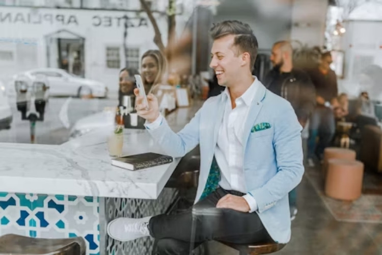 Homem sentado em mesa de restaurante usando o celular para acessar o Kismia