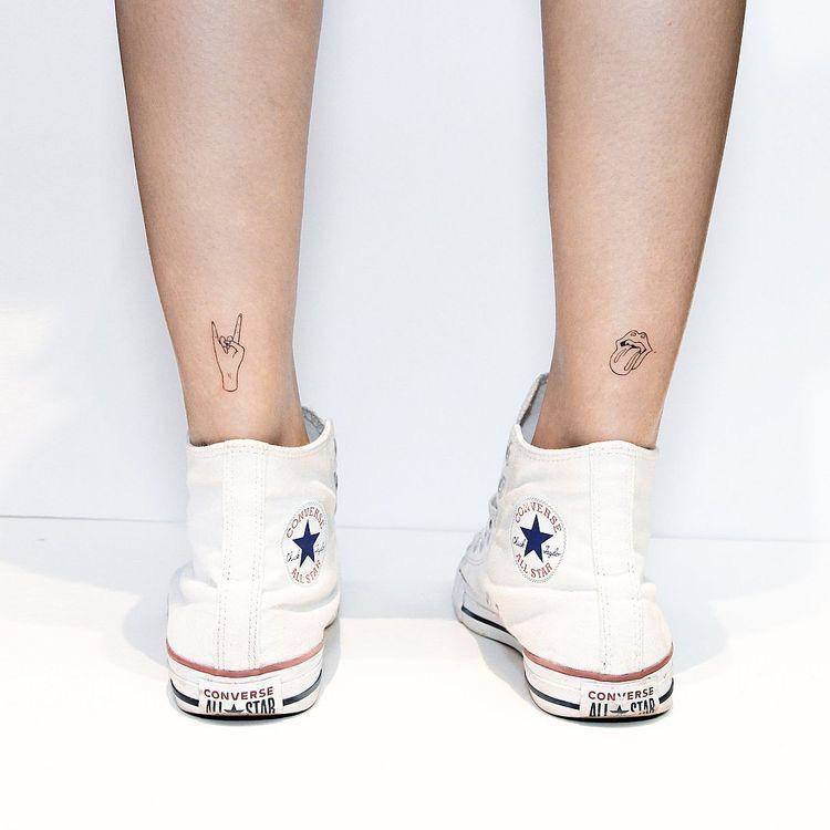 Tatuagem de rock n' roll na canela. Uma de símbolo do rock com os dedos e outra boca com língua do Rolling Stones