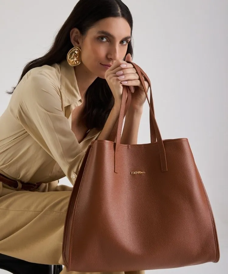 Modelo usando look bege e segurando bolsa de couro grande marrom da Move & Co