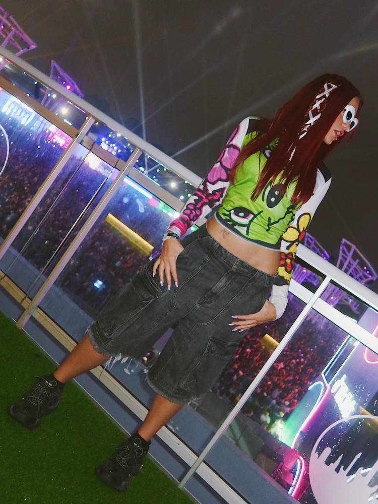 Vivi em festival de música usando bermuda jeans, tênis, blusa verde neon e óculos