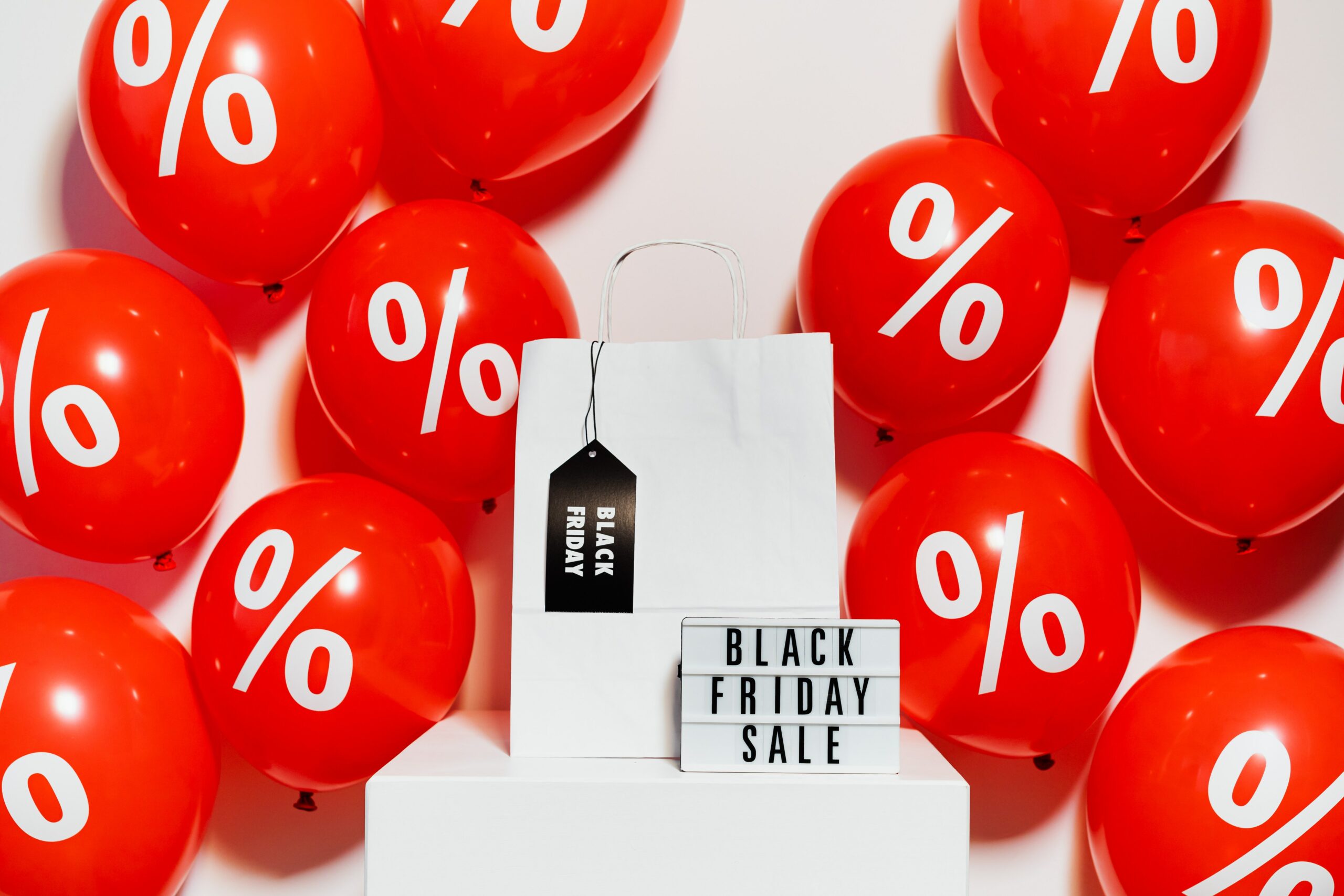 toten com bolsa branca, placa escrito Black Friday Sale e diversos balões vermelhos no fundo com desenho de porcentagem