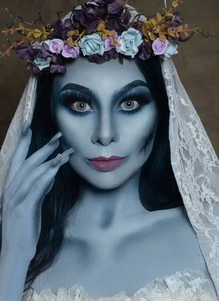 Mulher usando maquiagem de noiva cadáver, pintada de azul, com véu de renda branca