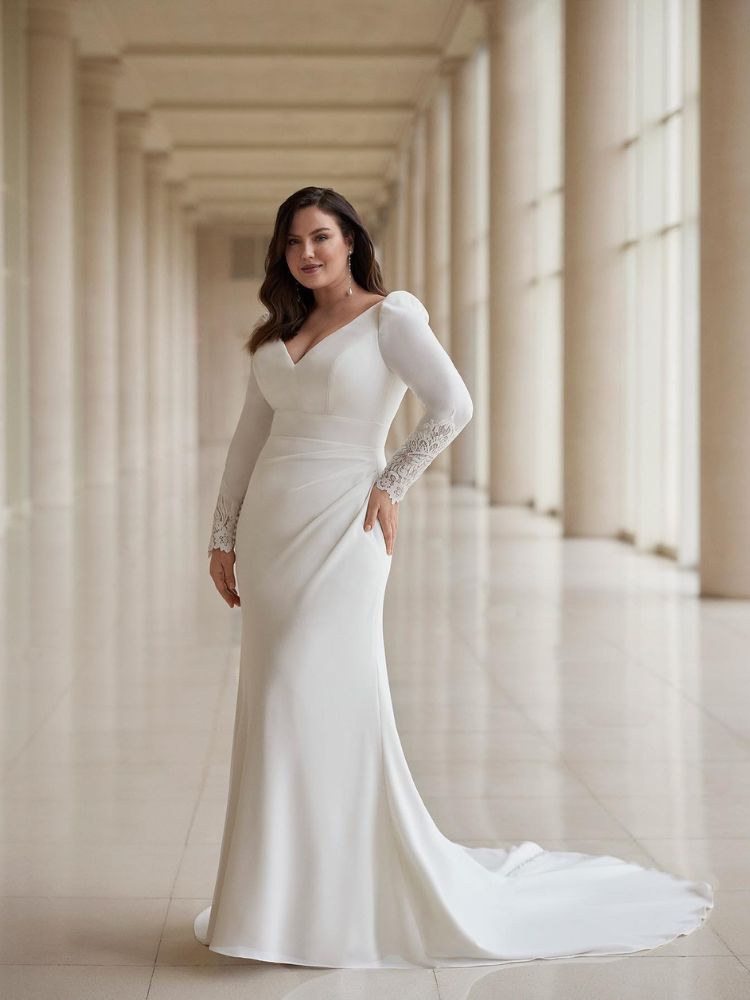 Mulher de pele clara usando vestido de noiva clean, sem muitos bordados, com decote e renda na manga