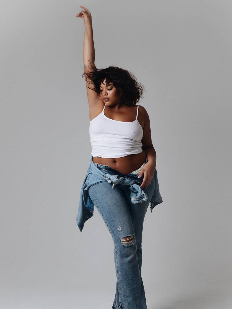 mulher usando regata branca, calça jeans rasgada e jaqueta jeans amarrada na cintura