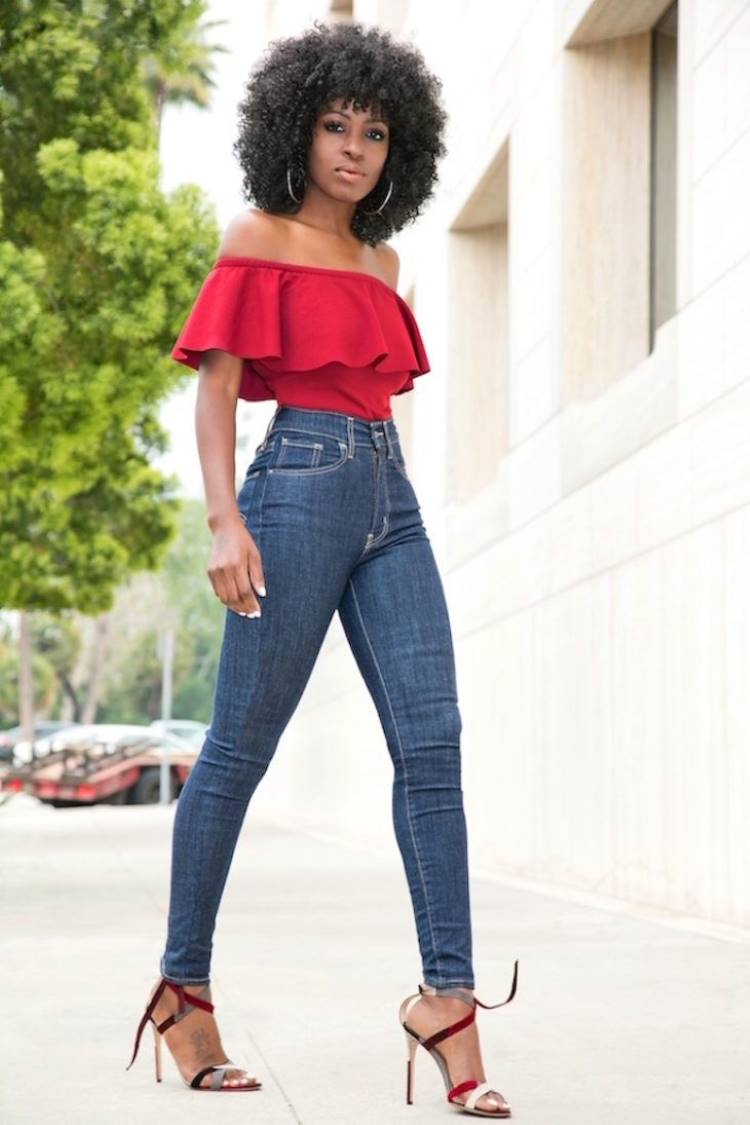Mulher de pele negra usando body ombro a ombro vermelho com babado e calça skinny cintura alta, além de sandália de salto