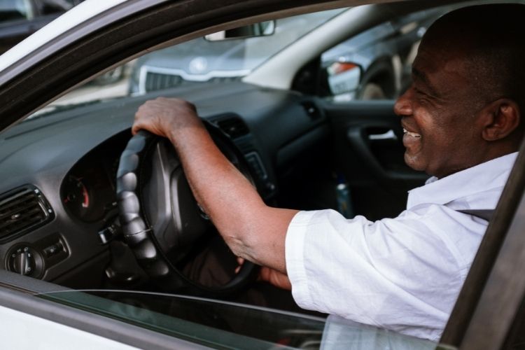 Imagem de um senhor negro dirigindo um carro. Ele aprece sorrindo. teste drive