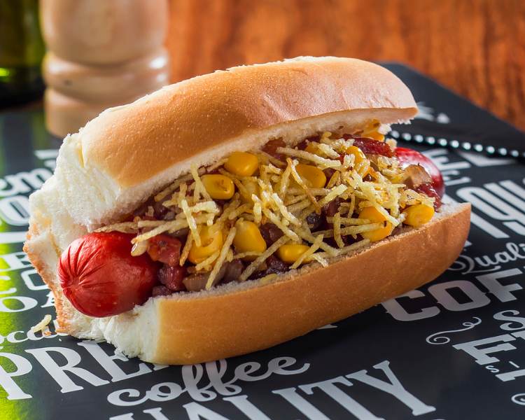 Cachorro-quente recheado com salsicha, bacon, milho, batata palha em tábua preta com palavras - receitas de festa junina