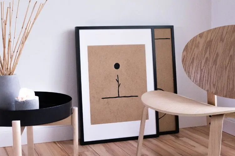Decoração escandinava com cadeira de madeira, mesa redonda preta e quadros no chão