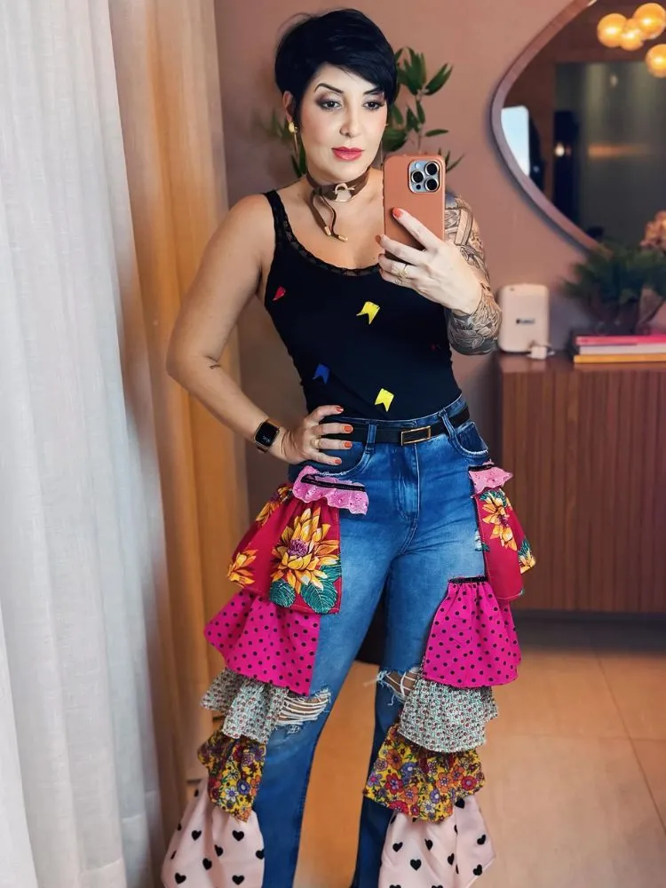 Mulher de pele clara de regata preta e calça jeans com lateral de retalhos de chita 