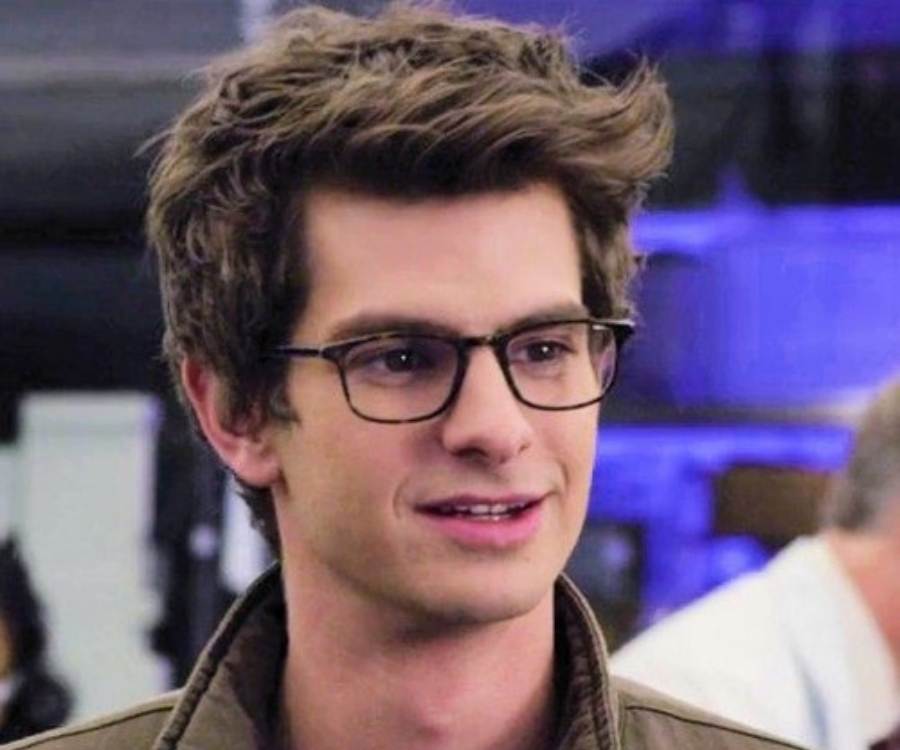 Andrew Garfield sorridente, usando óculos e jaqueta, em cena como Peter Parker.