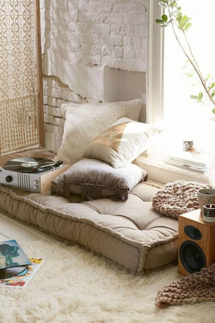 Espaço zen com tocador de disco, caixa de som, colchão cinza, almofadas, velas e plantas