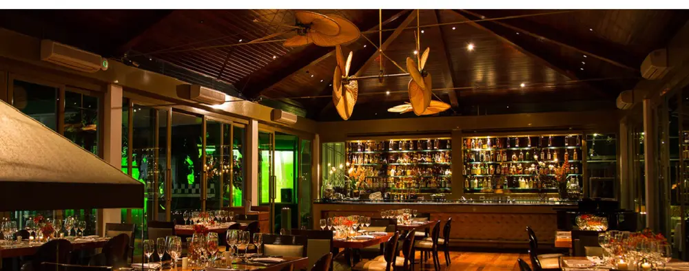 Área com paredes de vidro e bar. Interior do Unique Garden - Restaurantes icônicos em SP