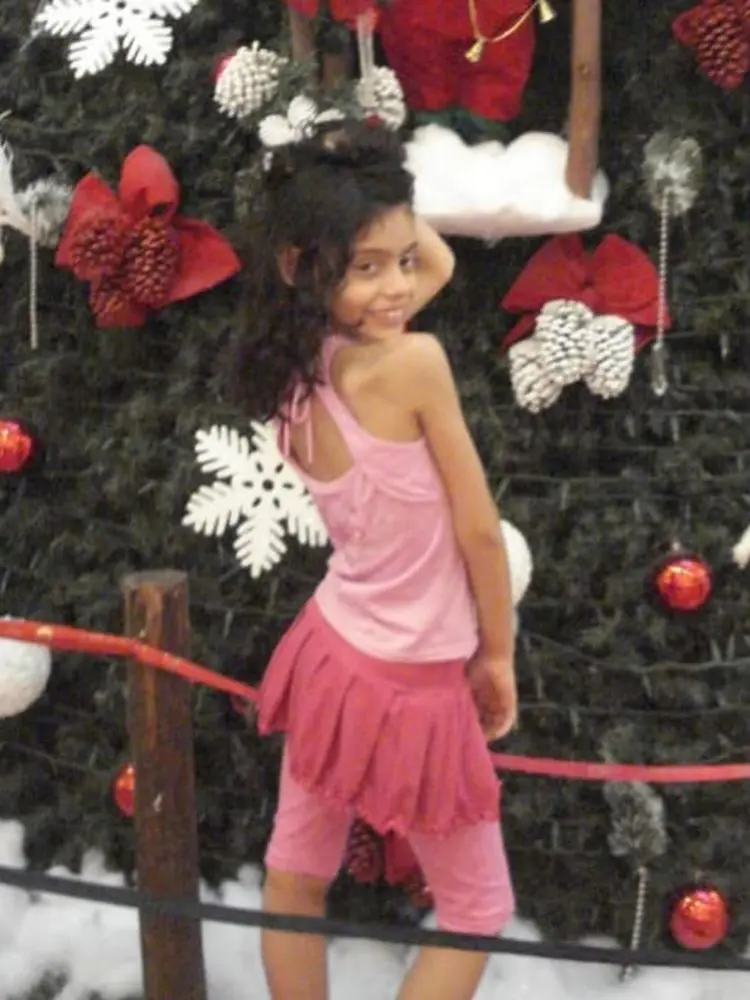 Menina Veneno criança de blusa, saia e calça rosas, posando em frente a uma árvore de Natal