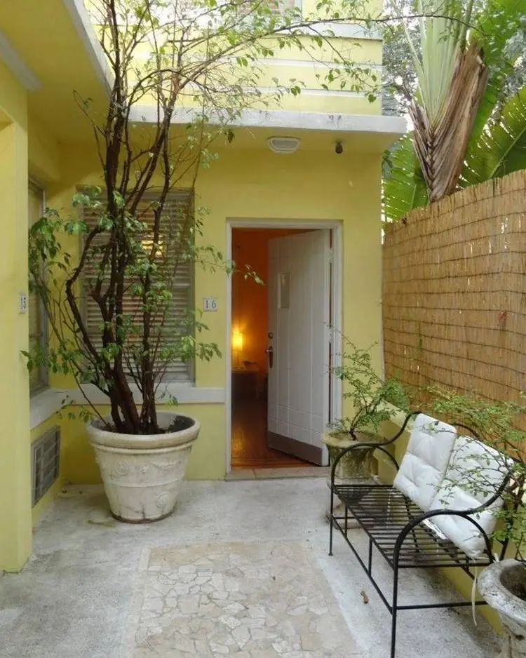 Quintal de casa com banco de ferro e grande vaso de planta.