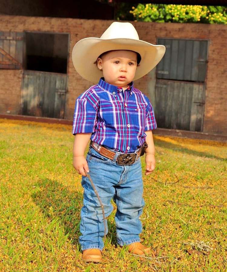 Menino usando chapéu de cowboy, camisa xadrez azul e vermelha, calça jeans e sapatão.
