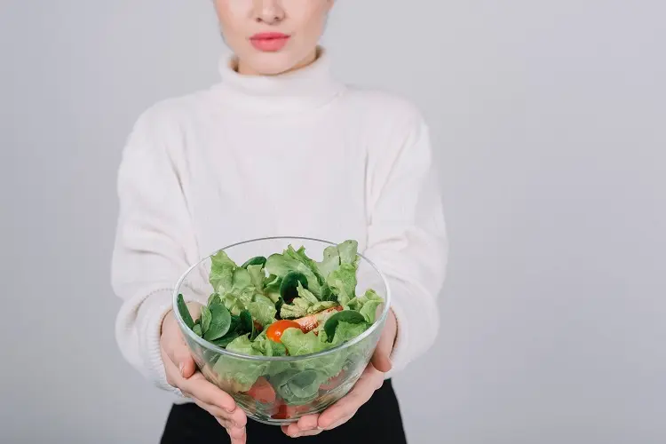 mulher segurando tigela de vidro com salada verde