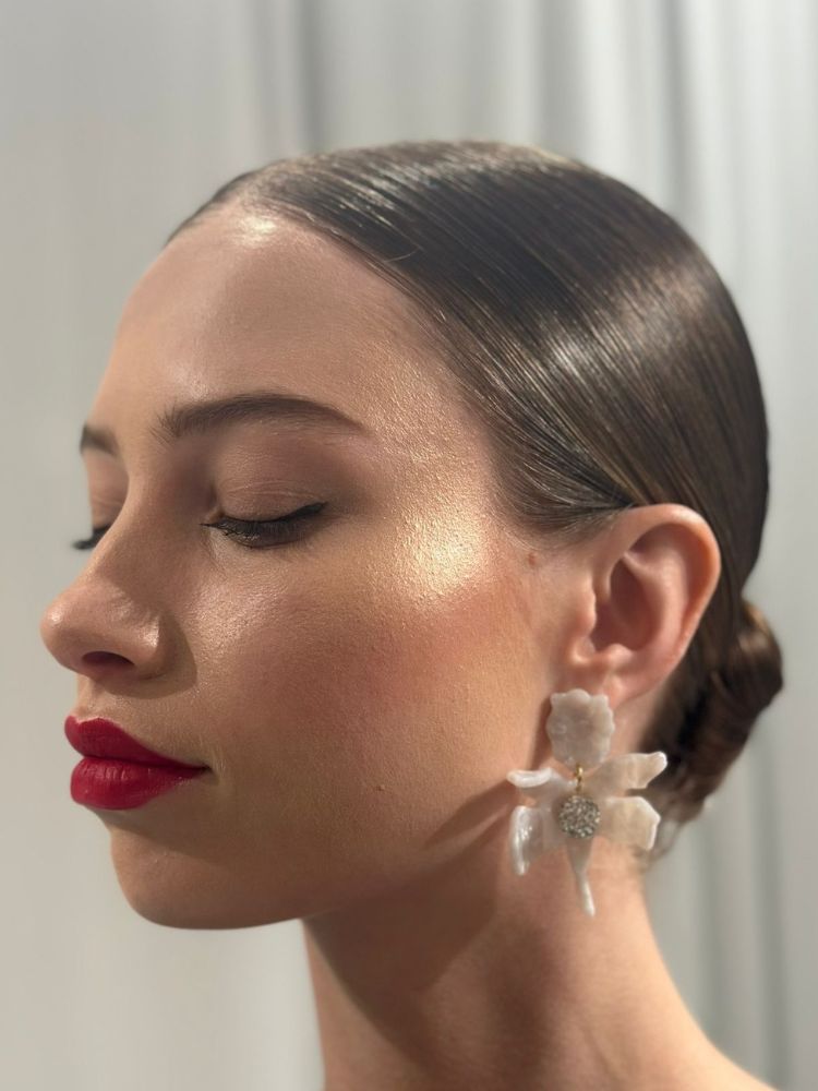 Mulher de pele clara usando coque baixo, brinco de flor e batom vermelho
