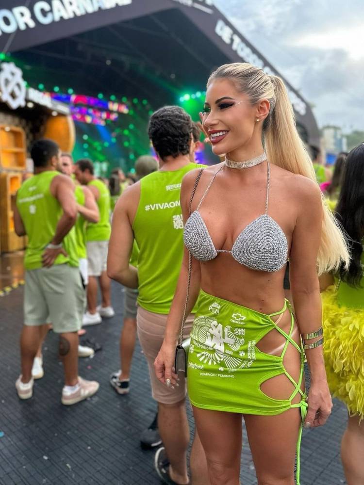 Mulher de pele clara e cabelo loiro na folia usando top de brilho e abadá verde transformado em saia. 
