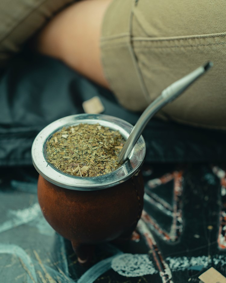 Chimarrão sob superfície ao lado de parte de braços de pessoa