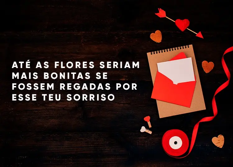 Foto de fundo marrom com caderneta, envelope, fita vermelha, prendedores de coração e coração flechado, além de frase "Até as flores seriam mais bonitas se fossem regadas por esse teu sorriso."