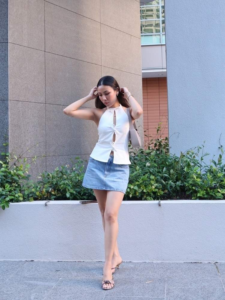 Mulher de pele clara usando blusa branca de amarração frontal e minissaia jeans