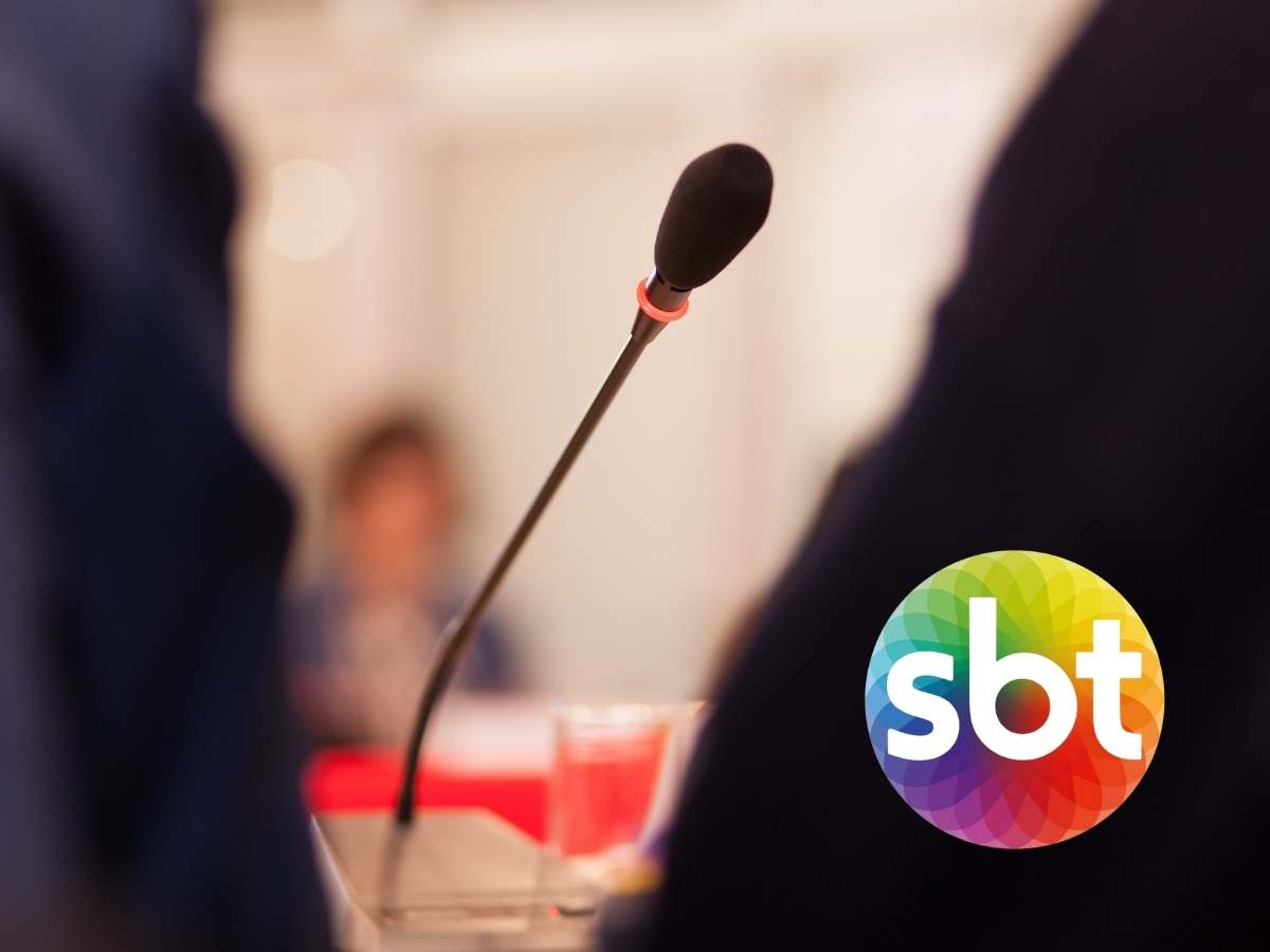 Foto de microfone em púlpito com pessoas ao lado e logotipo do SBT. 