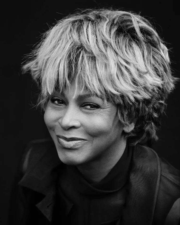 Cantora Tina Turner com cabelo curto, maquiada e usando roupa social em foto preto e branca