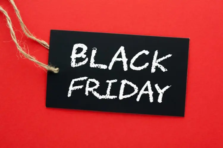 A imagem mostra uma etiqueta preta com as palavras "BLACK FRIDAY" escritas em letras brancas e grandes. A etiqueta está sobre um fundo vermelho vibrante e tem uma corda de juta presa a um canto, sugerindo que pode ser pendurada. O contraste entre o preto e o vermelho destaca a mensagem promocional.


