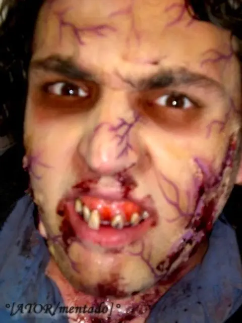 Homem usando maquiagem de halloween com veias, dentadura ensanguentada e machucados com sangue falso