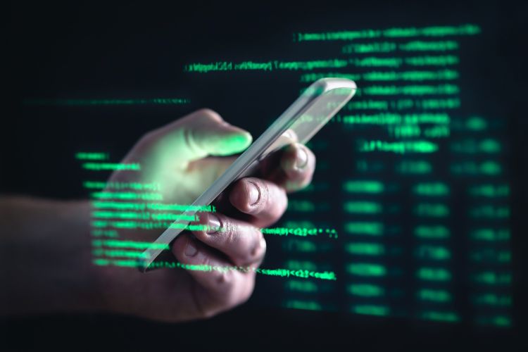 Mão segurando celular com fundo preto e códigos escritos de verdes