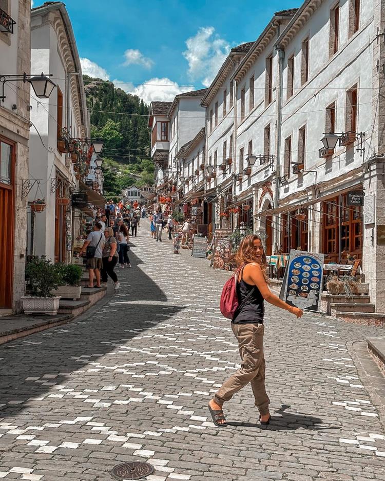 foto de mulher atravessando rua de pedra e prédios branco