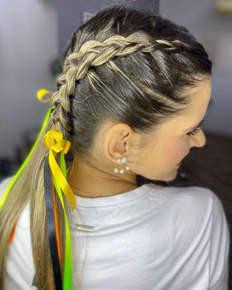 Cabelo loiro com duas tranças e fitas coloridas.