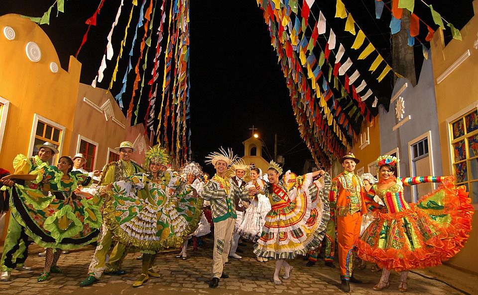 Pares de casal de dança quadrilha na rua de paralelepípedo, com bandeirinhas e prédios históricos
