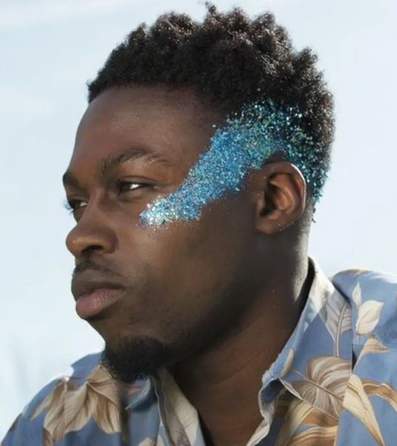 Homem de pele negra com maquiagem de glitter azul até o cabelo