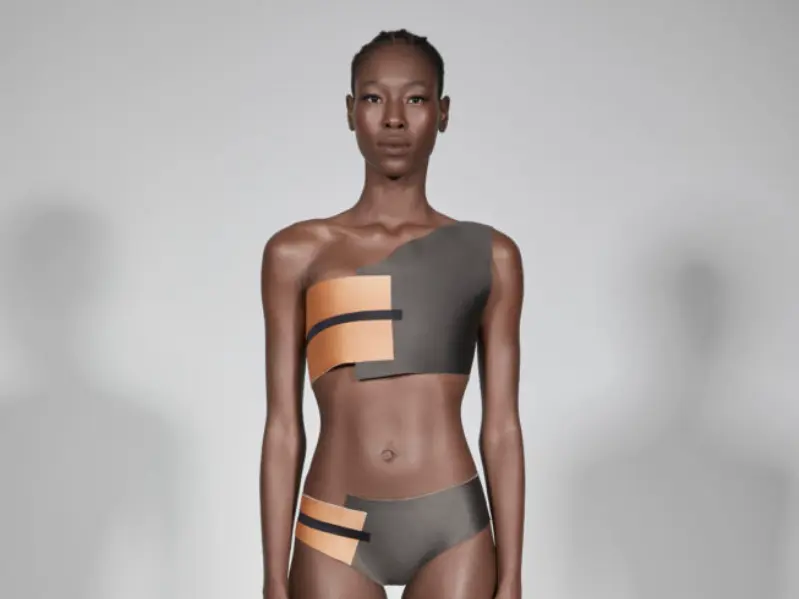 Modelo veste top e calcinha assimétricos com recorte laranja e cinza. 