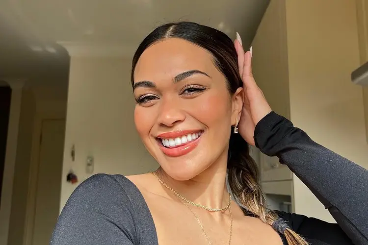 Mulher de pele morena sorrindo, usando maquiagem natural e blusa de manga longa preta 