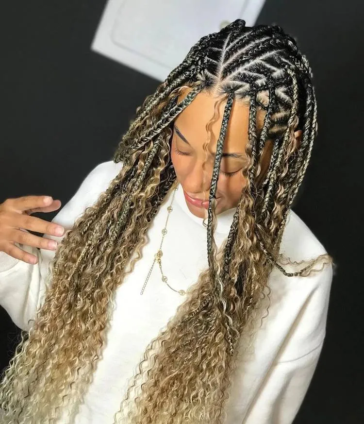 Mulher com a cabeça abaixada mostrando seu cabelo com trança nagô e box bradis. Ela usa moletom branco e colar dourado