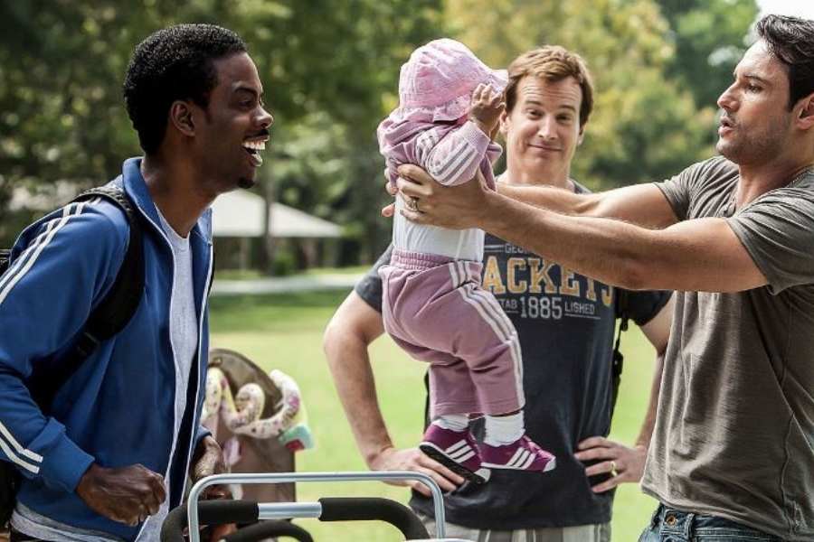 Foto de atores do filme "O que Esperar Quando Você está Esperando". 3 homens, um segura uma criança e os outros dois olham sorrindo.