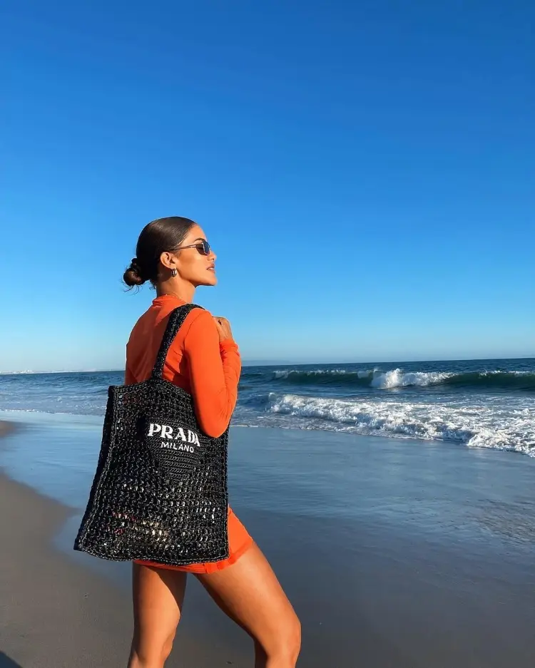 Camila Coelho na praia de saída laranja e bolsa de rede da Prada