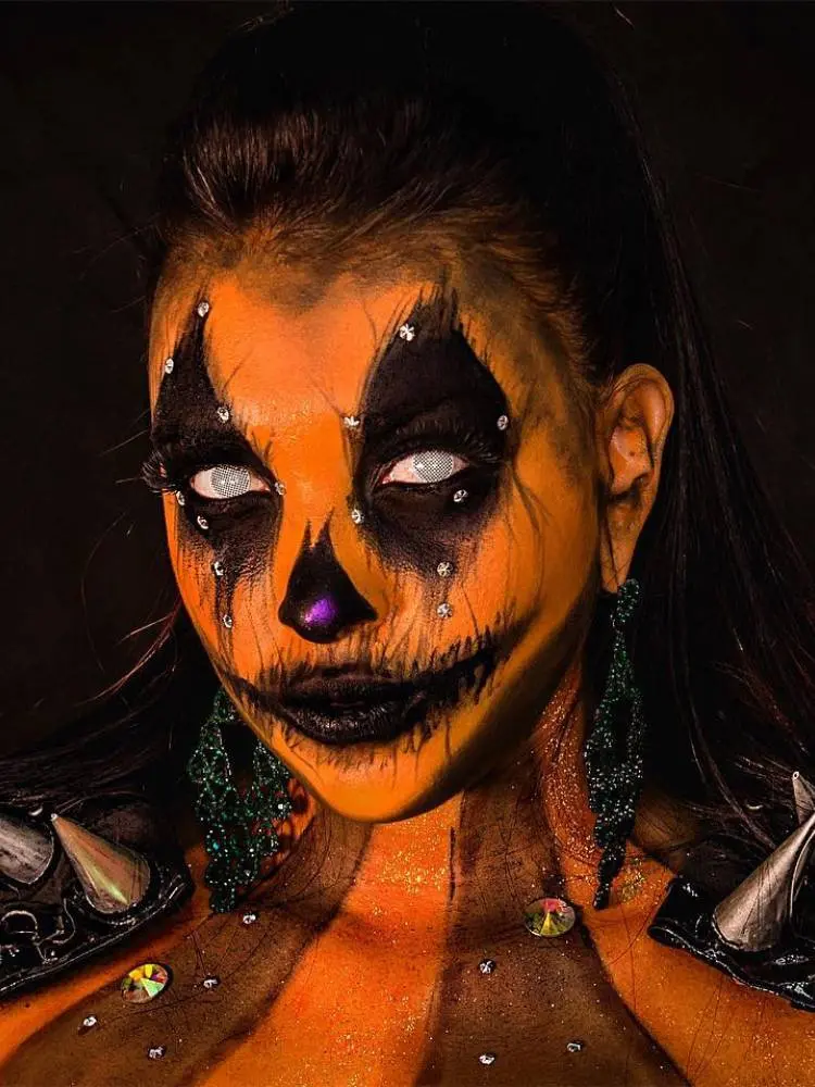 Mulher com maquiagem de abóbora, pintada de laranja e preto, com lentes brancas nos olhos