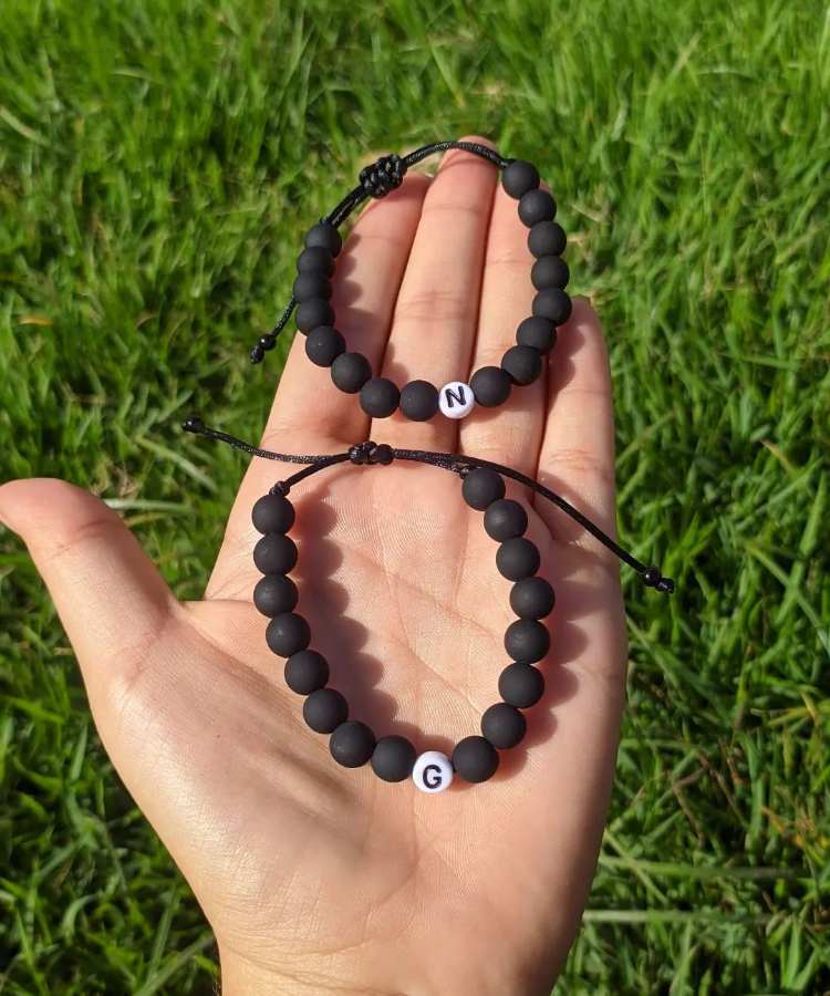 Mão segurando pulseira de miçangas preta e branca com letra inicial de casal