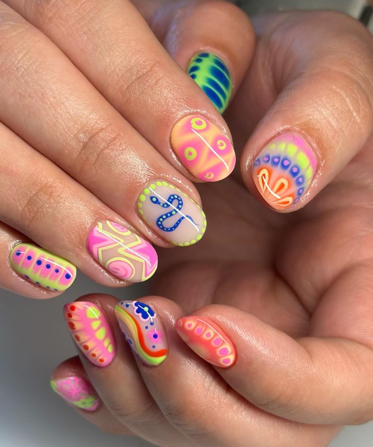 A imagem exibe unhas curtas e ovais decoradas com um design vibrante e furta-cor. As cores do arco-íris, como rosa, azul, amarelo e verde, são aplicadas em camadas onduladas e texturizadas, criando um efeito tridimensional brilhante.