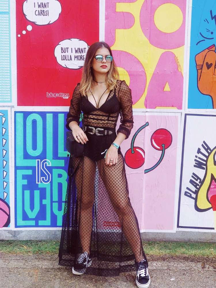 Mulher loira de pele clara em frente aos lambe-lambes do Lollapalooza usando hot pant preta, sutiã preto e vestido transparente preto