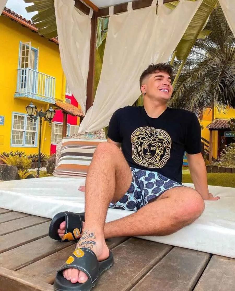 Foto de Lucas Santos sentado no chão mostrando sua tatuagem no pé