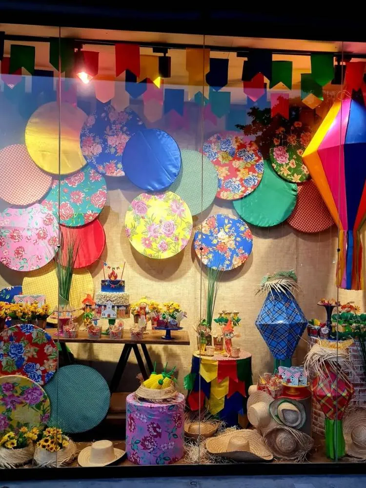 Vitrine decorada com balões, sousplats coloridos e enfeites juninos