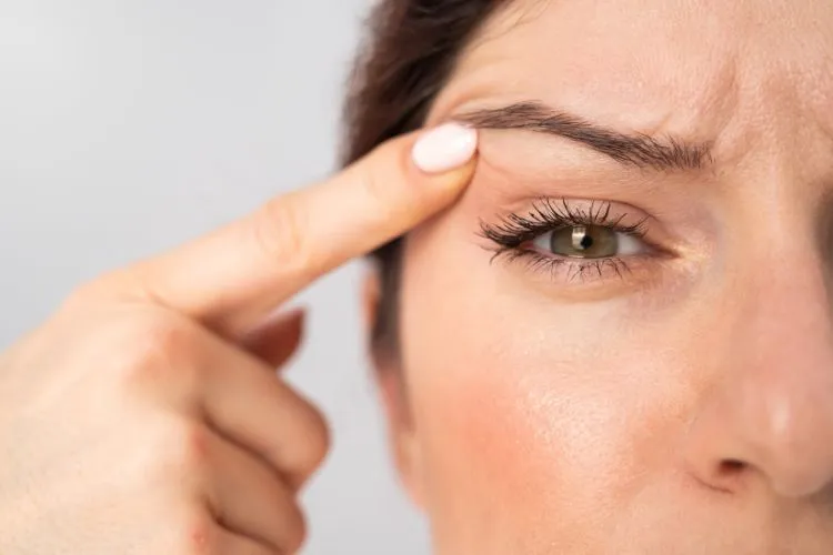 Mulher de pele clara e olhos esverdeados usando o dedo indicador para subir a pálpebra de um olho