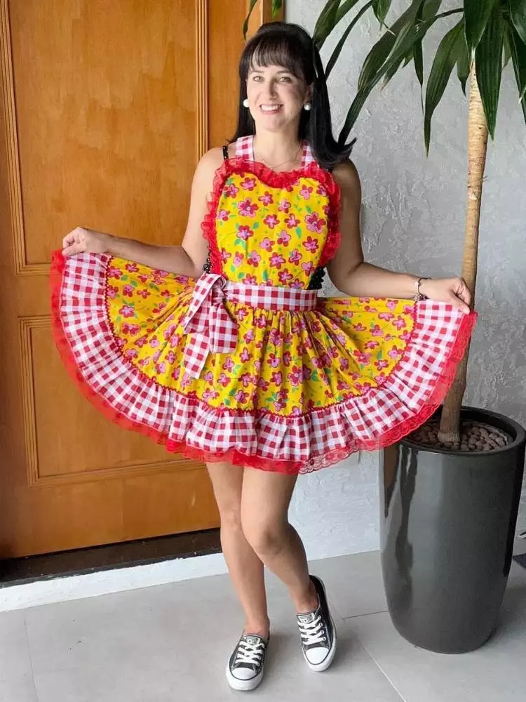 Mulher de pele clara usando avental junino amarelo, com tecido xadrez e renda vermelha