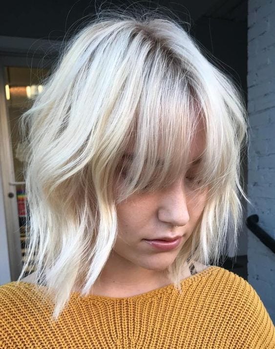 Mulher com cabelo curto platinado, usando casaco de lã caramelo
